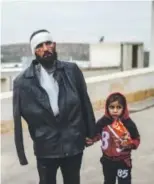  ??  ?? An injured Syrian man waits with his child outside a hospital after they crossed the border into Turkey.