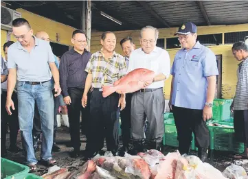  ??  ?? Uggah takes a closer look at a red snapper, which is among the fish landed at the landing facility in Muara Tebas. Also seen are Swee Kee Marine chief executive officer Chen Vui Phin (front second left) and operations general manager Lo Siaw Joo (front...