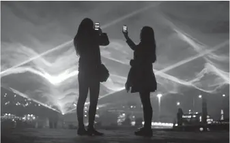  ??  ?? People take photos of the light display entitled Waterlicht by Daan Roosegaard­e at Granary Square in London, during the Lumiere London light festival.