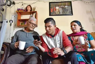  ?? HYOSUB SHIN / HSHIN@AJC.COM ?? Ryan Koirala (center) helps his parents, Tila (left) and Bhakti, operate a smartphone while they drink milk tea at their home in Clarkston.