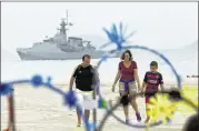 ?? SILVIA IZQUIERDO / ASSOCIATED PRESS ?? A family walks along Copacabana beach, with a Brazilian navy vessel just offshore, in Rio de Janeiro on Thursday. The country is beefing up security as the Olympics nears.