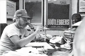  ?? File photo ?? ■ Arkansas filmmaker Charles B. Pierce is pictured in this 1983 file photo by the Texarkana Gazette. Film posters of two of his films, “Bootlegger­s” and “The Legend of Boggy Creek,” can be seen on the wall behind him. Pierce died in March 2010, and his daughter, Pamula Pierce Barcelou, has gained the copyright to “The Legend of Boggy Creek” and is having the movie restored for a future re-release, she said.