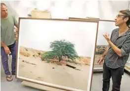  ??  ?? Art photograph­er Ron Amir (left) and curator Noam Gal stand next to a picture from the exhibition on migrants, “Somewhere in the Desert,” at the Israel Museum storage room in Jerusalem.