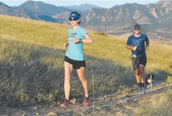  ?? Cliff Grassmick, Daily Camera ?? Kristin Gablehouse, left, her husband, Josh Lawton, and dog, Kili, go for a training run south of Boulder. Gablehouse suffered a brain injury after a cycling accident and has turned to ultramarat­hons to heal.