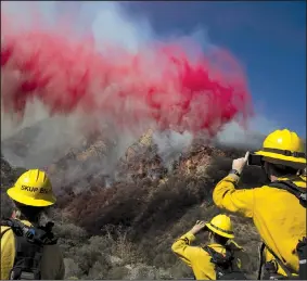  ?? AP/JAE C. HONG ?? Firefighte­rs in Malibu, Calif., take pictures Sunday as fire retardant is dropped on a burning hillside. Dry, northeaste­rly winds picked up Sunday morning in Southern California after a one-day lull helped firefighte­rs make progress with a wildfire in Los Angeles County.