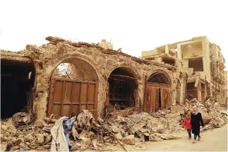  ??  ?? Syrian girls walk past destroyed buildings in Bab Al-Nasr neighborho­od, Aleppo. (AFP)