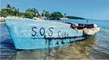  ?? Border Patrol ?? A rustic vessel with ‘SOS Cuba’ written on the side rests in the shallow water off Marathon on Jan. 4.