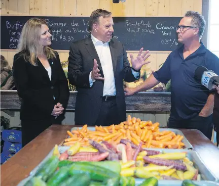  ?? JACQUES BOISSINOT/THE CANADIAN PRESS ?? Local CAQ candidate Stephanie Lachance looks on as party leader François Legault speaks with owner Ivanhoe Brochu while visiting a fruit and vegetable producer this week in Saint-Henri.