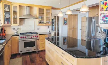  ??  ?? Above left, the efficient new kitchen, built around a Wolf stove, includes cabinets by John Newell installed 17 years ago. They are maple with shaker-style stain and mitred doors for a clean look. Countertop­s are black granite with flecks of blue. The new pantry is a cabinet on wheels, far right, which rolls out to reveal the hot-water heater. At right, Jim updated a cast aluminum bistro set by spraying it with a vivid shade of Tremclad blue. Behind is a scarlet rhodo, while hyacinths and allium sit in a purple pot.