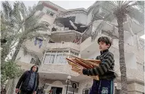  ?? AFP PHOTO ?? SIGN OF STRIKE
A Palestinia­n boy carrying pieces of wood walks near a partially destroyed residentia­l building following fresh Israeli bombardmen­t in the city of Rafah, southern Gaza Strip on Saturday, Feb. 10, 2024.