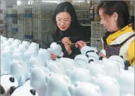  ?? LI HONGTU / FOR CHINA DAILY ?? In a factory in Dehua, Fujian, a worker (right) demonstrat­es the ceramic version of the doll to a reporter.