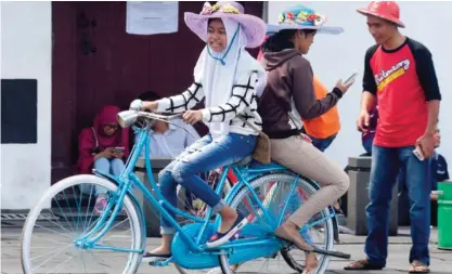  ??  ?? JAKARTA: A youth ferries a friend on a rented bicycle on the main square of Jakarta’s old town. — AFP