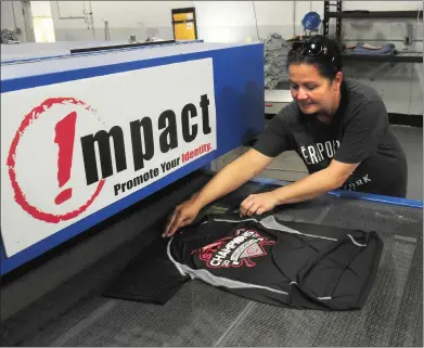  ??  ?? Melissa Machado, of Impact Custom Apparel in Cumberland, picks up one of the Cumberland American practice jerseys as it exits the dryer on Friday.