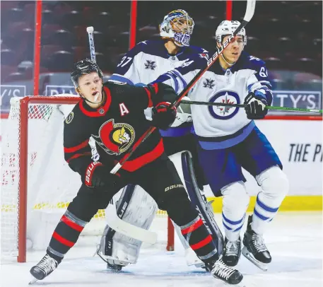  ?? ERROL McGIHON ?? The Senators' Brady Tkachuk checks Winnipeg Jets defenceman Logan Stanley in front of Jets goaltender Connor Hellebuyck during the first period Thursday evening at Canadian Tire Centre.