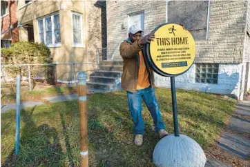  ?? BRIAN CASSELLA/CHICAGO TRIBUNE PHOTOS ?? Homeowner George Parker picks up a sign about the legacy of contract sales in the 6500 block of South Aberdeen Street, where he lives, on Dec. 11. The home was owned by Dock and Johnella Walls, who endured an unjust land sale contract in 1963. Several buildings on the block are receiving funding for rehab projects through the “unBlocked Englewood” project.