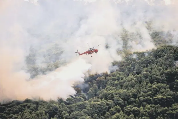  ?? PICTURE: AFP/GETTY IMAGES ?? 0 A firefighti­ng helicopter drops water over part of a wildfire near Athens, as the death toll rose to at least 79, with hundreds more injured