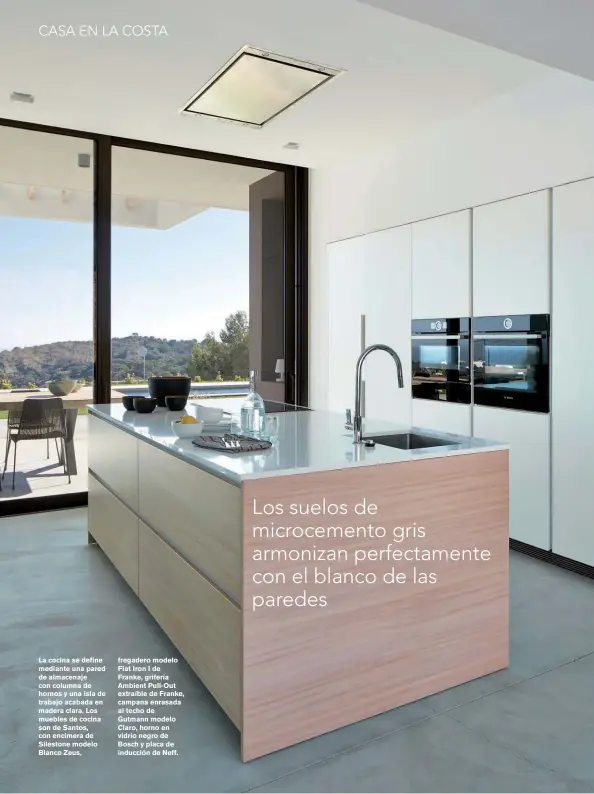  ??  ?? La cocina se define mediante una pared de almacenaje con columna de hornos y una isla de trabajo acabada en madera clara. Los muebles de cocina son de Santos, con encimera de Silestone modelo Blanco Zeus, fregadero modelo Flat Iron I de Franke, grifería Ambient Pull-Out extraíble de Franke, campana enrasada al techo de Gutmann modelo Claro, horno en vidrio negro de Bosch y placa de inducción de Neff.