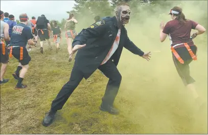  ?? DANA JENSEN/THE DAY ?? Runners try to avoid a zombie, Chris Busse of Ashford, at the start of Saturday’s Zombie Charge, a 5K mud run featuring obstacles and zombies trying to pluck flags from their belts. The event at Suchocki Tree Farm in North Stonington raised money for...