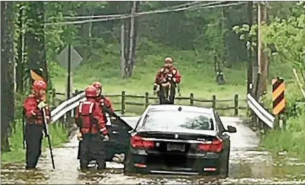  ?? SUBMITTED PHOTO – WEST PIKELAND POLICE ?? Lionville firefighte­rs assist the driver of this BMW which was stalled in flood waters on Horseshoe Trail at the Pickering Creek Thursday morning.