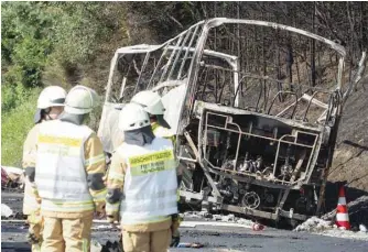  ?? — AFP ?? Members of the fire brigade work at the scene where a tour bus burst into flames following a collision with a trailer truck on the highway A9 near Muenchberg, southern Germany, on Monday.