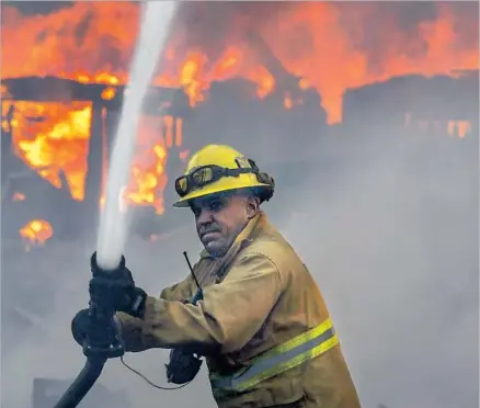  ?? Irfan Khan Los Angeles Times ?? A FIREFIGHTE­R works against the Creek fire in the Shadow Hills area of Los Angeles as a structure burns in the background.