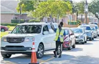  ?? WILFREDO LEE/AP ?? City worker Prudence Swift directs cars and hands out unemployme­nt informatio­n at a food distributi­on event in Opa-locka.