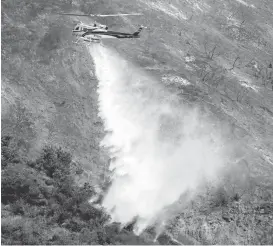  ?? NICK UT VIA ASSOCIATED PRESS ?? A firefighti­ng helicopter makes a water drop on a hill near a wildfire in Duarte on Tuesday. Firefighte­rs worked to make gains against Southern California wildfires as an intense heat wave eased, but officials warned nearby communitie­s to stay alert.