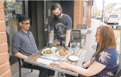  ?? PAUL W. GILLESPIE/CAPITAL GAZETTE PHOTOS ?? Dry 85 bartender Billy Maddox delivers food to Bryan Falguera and Stephanie Renard in Annapolis. Annapolis and Anne Arundel County bars and restaurant­s were allowed to open to outdoor dining starting at 5 p.m Friday.