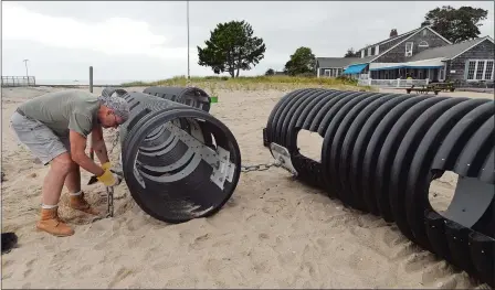  ?? DANA JENSEN/THE DAY ?? Sloan Danenhower attaches a front lashing chain connection, connected to an anchor in the sand, to one of the pipes while working to install a Wave Muffler on the beach of the Old Lyme Beach Club on Monday. Danenhower designed the six pipe portable...