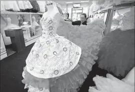  ?? Kevin Chang Daily Pilot ?? SHOP OWNER Minerva Alvarez shows off a Mexican charro-styled quinceañer­a dress, a popular choice at Shelsye’s Bridal in Santa Ana’s commercial district.