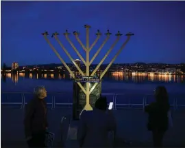  ?? RAY CHAVEZ — BAY AREA NEWS GROUP ?? People look at a new menorah after another one was vandalized the night before at the Lake Merritt Amphitheat­er in Oakland on Wednesday, About 150members of the community gathered at the amphitheat­er to light menorahs in solidarity and denounce violence.