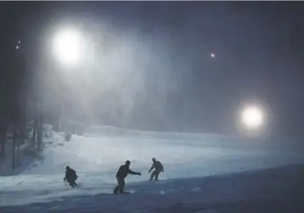  ?? Andy Cross, The Denver Post ?? A skier and snowboarde­rs head down the slope under the lights during a heavy snowstorm at the Keystone Resort.