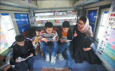  ?? RAHMAT GUL / ASSOCIATED PRESS ?? Owner of the bus library Freshta Karim (right) helps children to read books inside her bus in Kabul, Afghanista­n, on Mar 10.