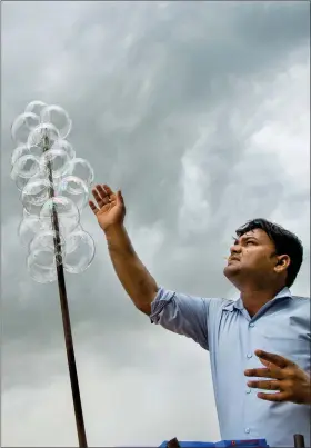  ?? A street vendor places bubbles from a bubble kit he offers for sale near the India Gate Monument as storm clouds gather above New Delhi on Thursday. AFP ??