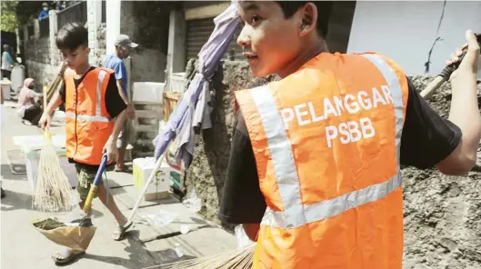  ?? SALMAN TOYIBI/JAWA POS ?? SANKSI SOSIAL: Warga yang melanggar aturan PSBB diminta membersihk­an sampah di Pasar Mampang, Jakarta, dengan mengenakan rompi khusus kemarin (14/5).