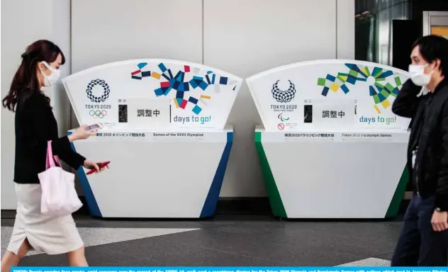  ?? — AFP ?? TOKYO: People wearing face masks, amid concerns over the spread of the COVID-19, walk past a countdown display for the Tokyo 2020 Olympic and Paralympic Games with notices which read in Japanese “Under adjustment” in Tokyo yesterday.