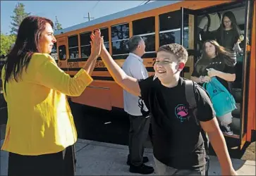  ??  ?? VICE PRINCIPAL Jillian Damon greets students with high-fives as they step off the school bus. Recognizin­g the magnitude of the homecoming, teachers mostly put off teaching for the day, in favor of hugs and reunions.