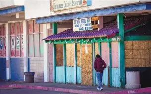  ?? CHANCEY BUSH/JOURNAL ?? A person walks past boarded-up windows at Franklin Plaza on Juan Tabo and Central.