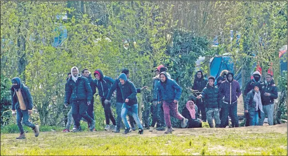  ??  ?? A gang of migrants emerge from their secret camp hidden in woodland close to the motorway services to try to force their way aboard UK-bound lorries