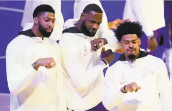  ?? Marcio Jose Sanchez / Associated Press ?? The Lakers’ Anthony Davis ( left) LeBron James and Quinn Cook show off their championsh­ip rings. The raising of the banner honoring their 17th title will wait until fans are in the stands.