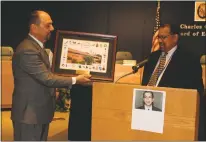  ?? STAFF PHOTO BY JAMIE ANFENSON-COMEAU ?? Paul Balides, outgoing assistant superinten­dent of finance for Charles County Public Schools, is presented with a framed photo of the Jesse L. Starkey Administra­tion Building by Randy Sotomayor, executive director of the Office of Finance and Business....