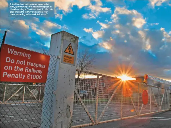  ?? ALAMY. ?? A Southeaste­rn train passes a signal hut at dusk, approachin­g a trespass warning sign at a level crossing in Chartham, Kent. A child risks their life on the railway tracks every four hours, according to Network Rail.