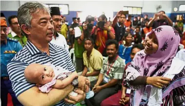  ??  ?? Meeting the people: Tengku Abdullah carrying a baby whose family was affected by the flood as her mother looks on during his visit to the relief centre in Kampung Pia. — Bernama