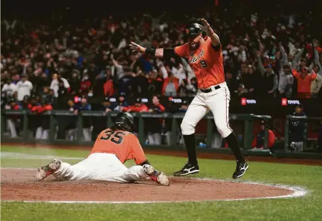  ?? Jeff Chiu / Associated Press ?? Brandon Crawford slides home, to Brandon Belt’s approval, with the winning run on Kevin Gausman’s sacrifice fly Friday night.