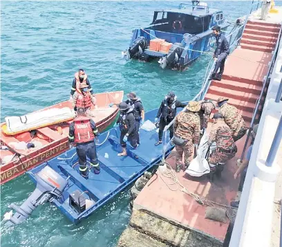  ??  ?? LEMAS: Pasukan bomba mengangkat mayat salah seorang mangsa selepas ditemukan terdampar di pantai.