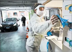  ??  ?? Registered nurse Alexis Hoogendoor­n grabs disposable gloves as people drive in for COVID-19 testing Thursday, in the indoor parking lot at the Lurie Children’s Hospital outpatient center.