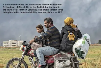  ??  ?? A Syrian family flees the countrysid­e of the northeaste­rn Syrian town of Ras al-Ain on the Turkish border west to the town of Tal Tamr on Saturday. The smoke is from tyres being burned to impede visibility from warplanes. — AFP