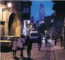  ??  ?? Pedestrian­s walk on a cobbled street as the Flame Towers stands in the background in the Old City of Baku, Azerbaijan, where east meets west.