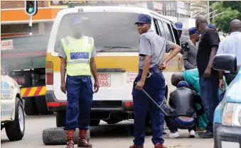  ??  ?? Traffic police stand guard while a kombi crew changes a punctured tyre at the intersecti­on of Herbert Chitepo Street and 9th Avenue in Bulawayo yesterday. Traffic police threw spikes under the moving kombi which was carrying passengers