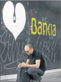  ?? Picture: REUTERS ?? NO LOVE LOST: A man kneels under a Bankia bank logo. Shares in the bank were suspended on the Madrid stock exchange on Friday.